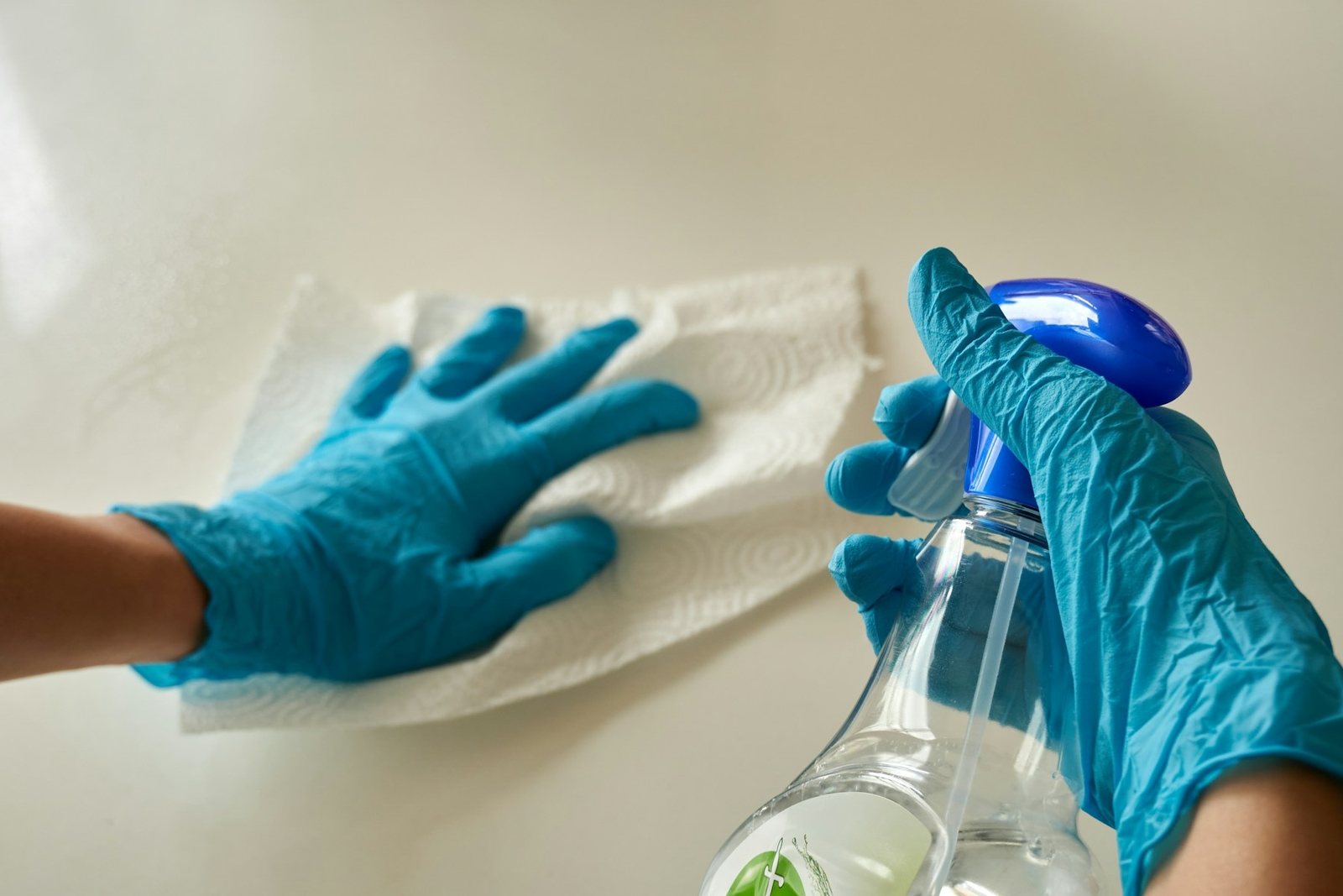 Gloved hand wiping a surface with cleaning spray